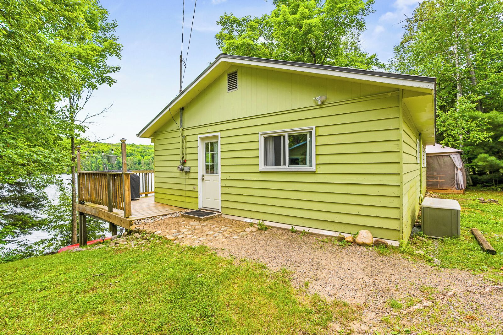 A small, single-story cabin with a deck, a door, and a window, located near a body of water.