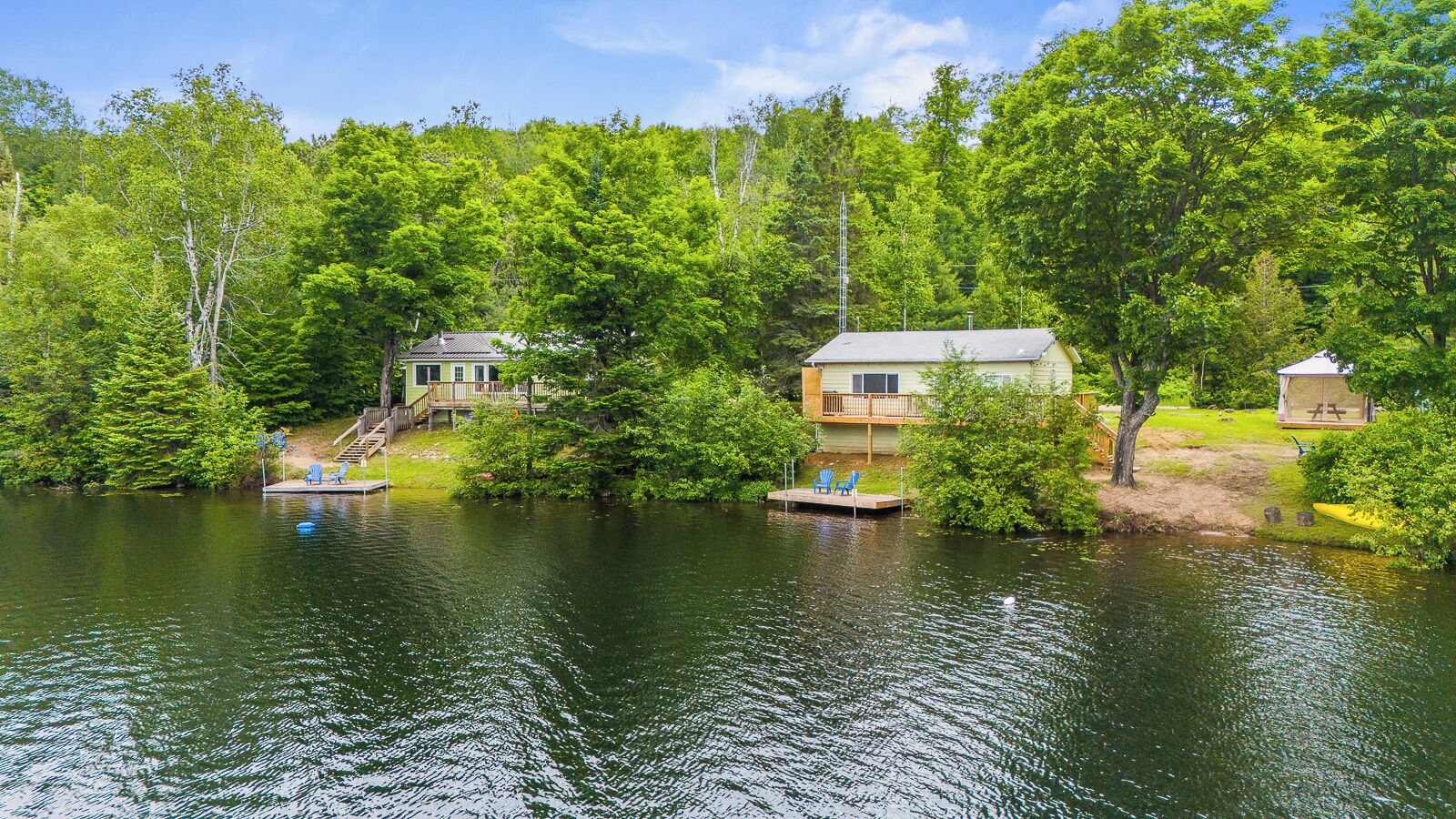 Un chalet au bord du lac, doté d’une jetée et de chaises, et entouré d’une végétation luxuriante.