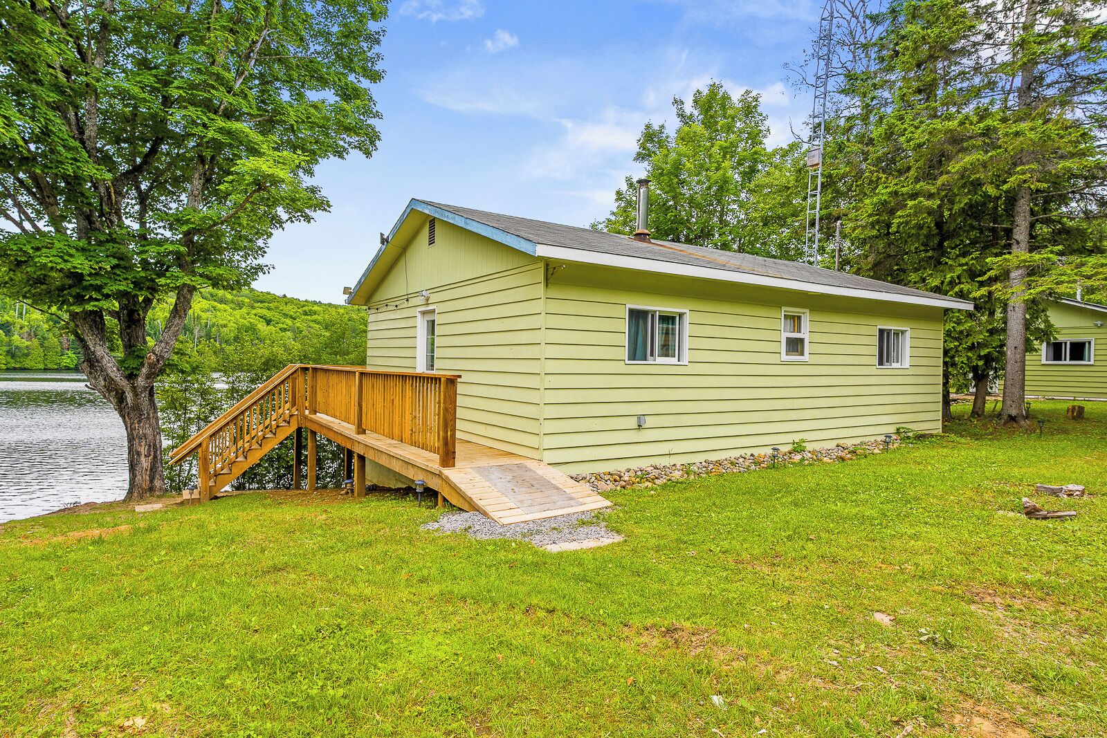Une petite cabane vert clair, dotée d’une terrasse en bois et d’un petit escalier menant à une porte.