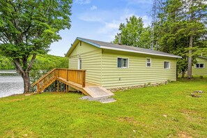 A light green cabin with a wooden deck and a small staircase leading to a door. - Two Peaceful Lakefront Cottages on beautiful Cardiff Lake. Perfect for families. (Harcourt)