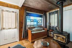 A cozy living room with a sofa, a fireplace, and a TV displaying streaming services. - Two Peaceful Lakefront Cottages on beautiful Cardiff Lake. Perfect for families. (Harcourt)