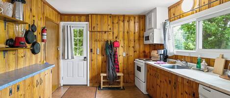 Una cocina compacta con paredes de madera, una puerta blanca y una ventana con vista a la vegetación.