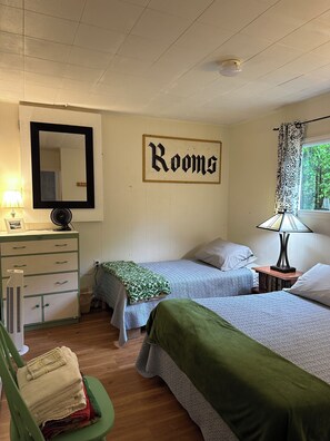 A room with two beds, a dresser, a mirror, a sign reading 'Rooms', and a window with curtains. - Two Peaceful Lakefront Cottages on beautiful Cardiff Lake. Perfect for families. (Harcourt)