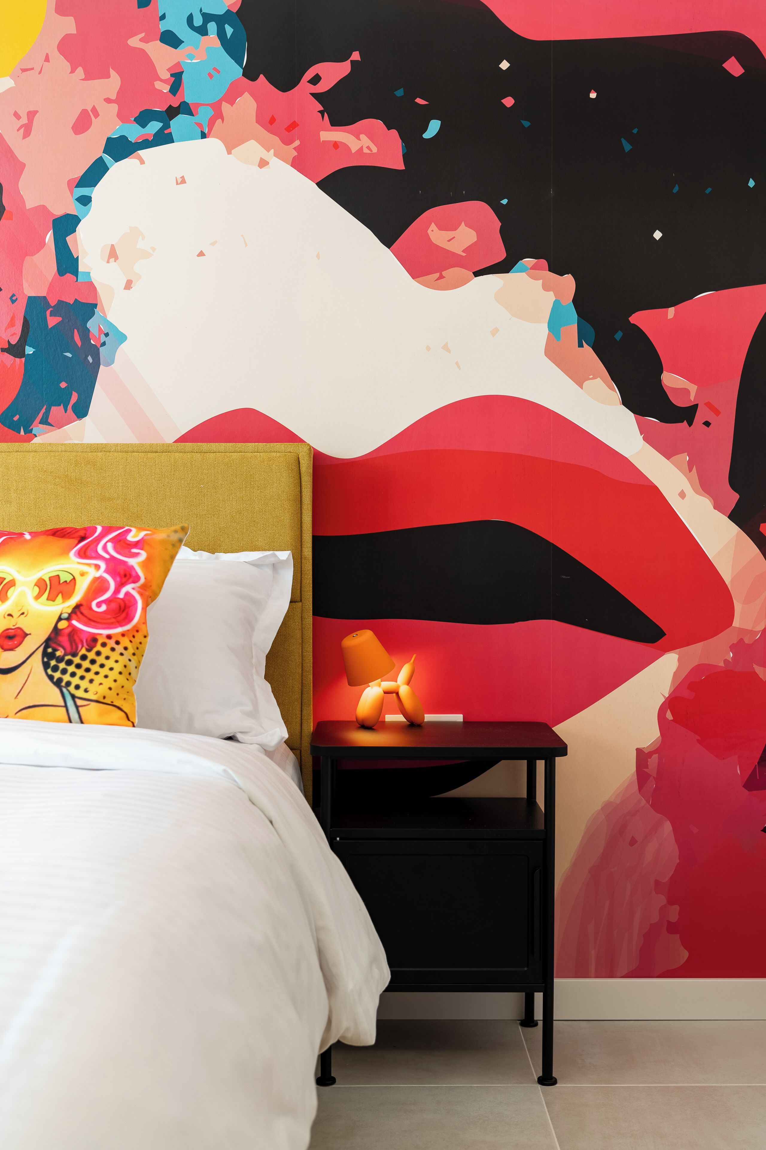Een slaapkamer met een bed, een nachtkastje en een muur met abstracte kunst.