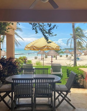 Eine Außenpatio mit Tisch und Stühlen, einem gestreiften Sonnenschirm und Blick auf Strand und Meer.