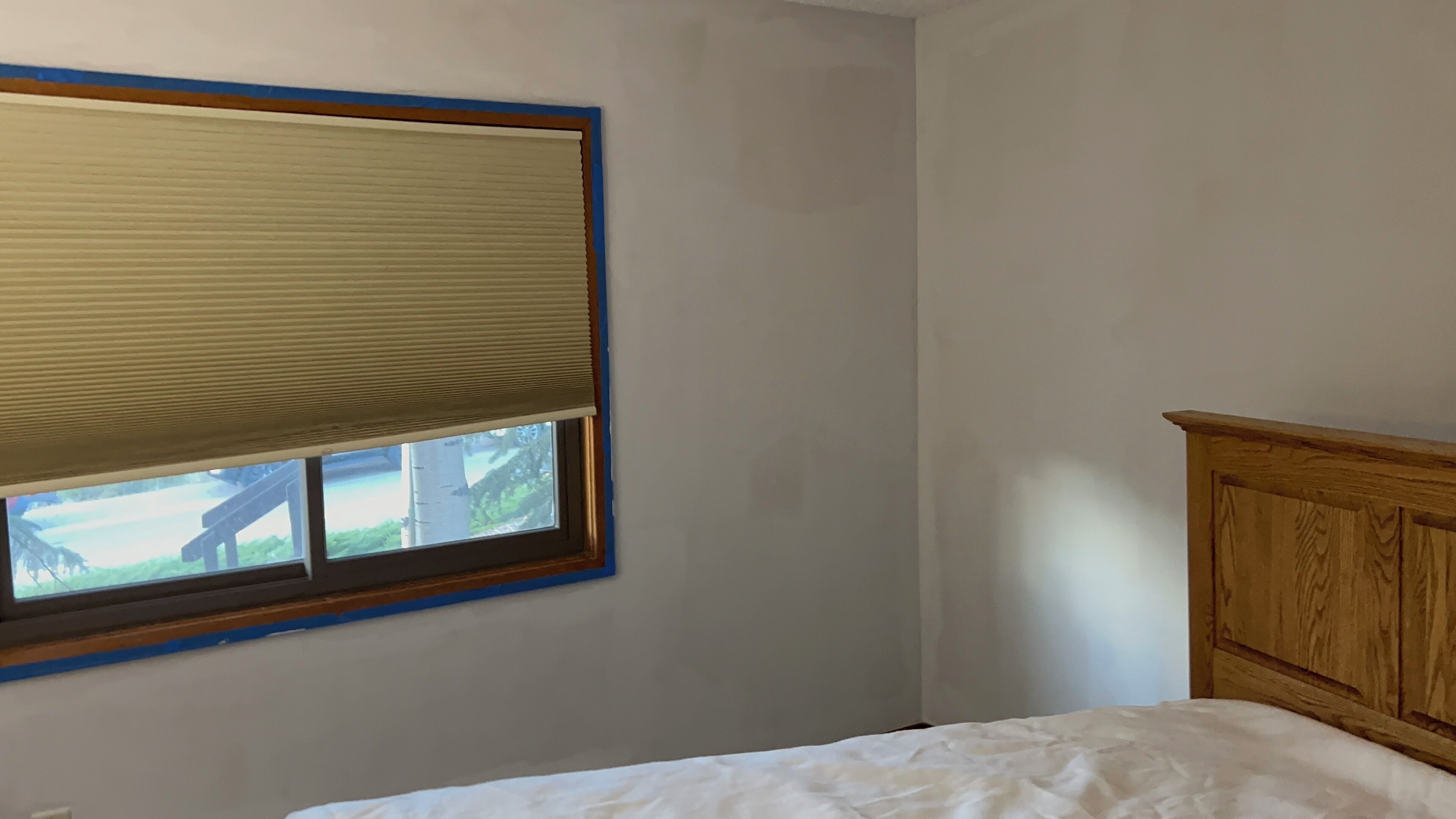 A bedroom with a single bed, a wooden headboard, and a window with blinds.
