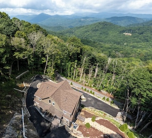 A house with a sloped roof, surrounded by a forested area with a road leading to it. - Blue Ridge Mountains View - House & Resort (Boone)