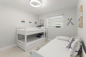 A child's bunk bed with a desk underneath, a single bed with matching bedding, and a window with blinds.