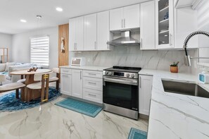 Una cocina moderna con armarios blancos, horno empotrado y un comedor con mesa y sillas redondas.
