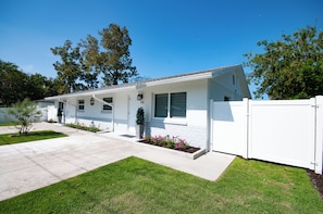 A single-story house with a front porch, a small garden, and a white fence.