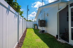 A narrow backyard with a white fence, a small grassy area, and a water heater on a stand.