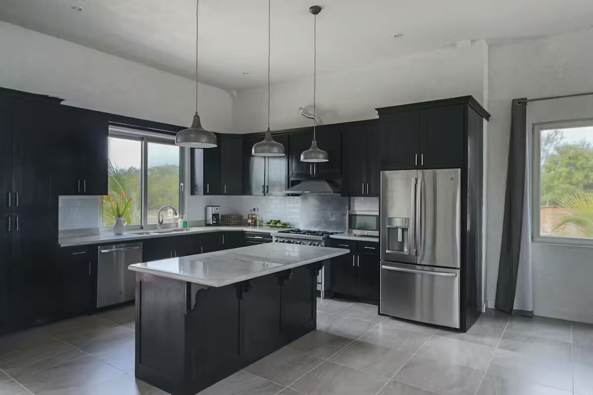 A modern kitchen with dark cabinetry, stainless steel appliances, and pendant lighting.