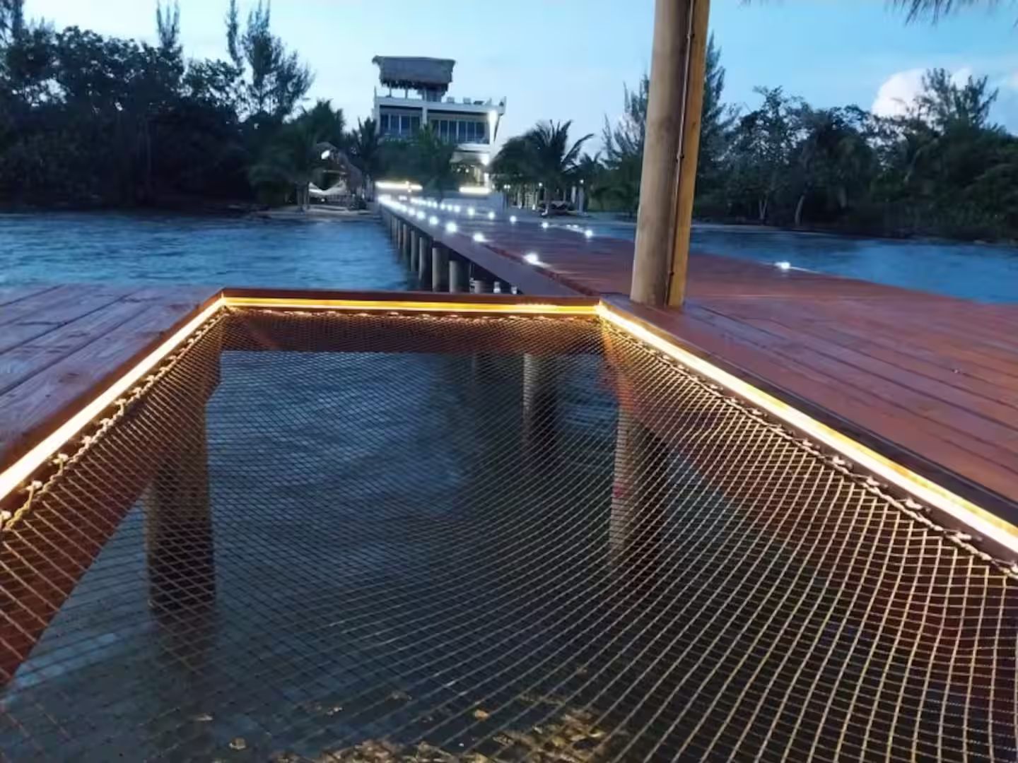 A wooden deck with a mesh barrier, leading to a building with a thatched roof.