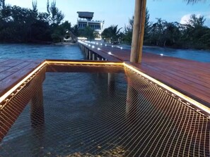 Una terraza de madera con una barandilla de malla que conduce a un edificio con techo de paja.
