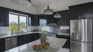 A modern kitchen with dark cabinets, stainless steel appliances, and a marble island with fruits.
