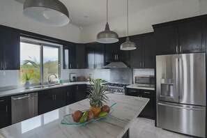 A modern kitchen with dark cabinets, stainless steel appliances, and a marble island with fruits.