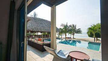 A poolside area with a thatched-roof structure, lounge seating, and a view of the beach.