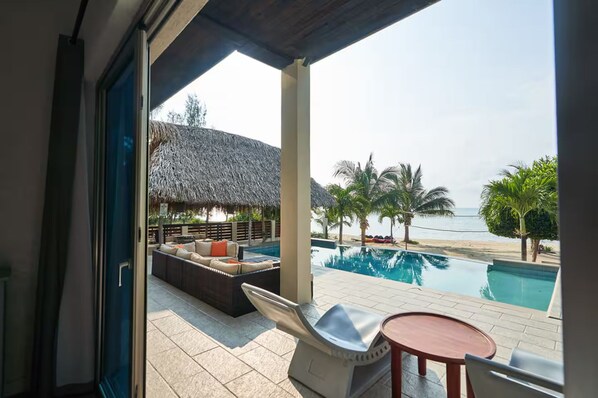 A poolside area with a thatched-roof structure, lounge seating, and a view of the beach.