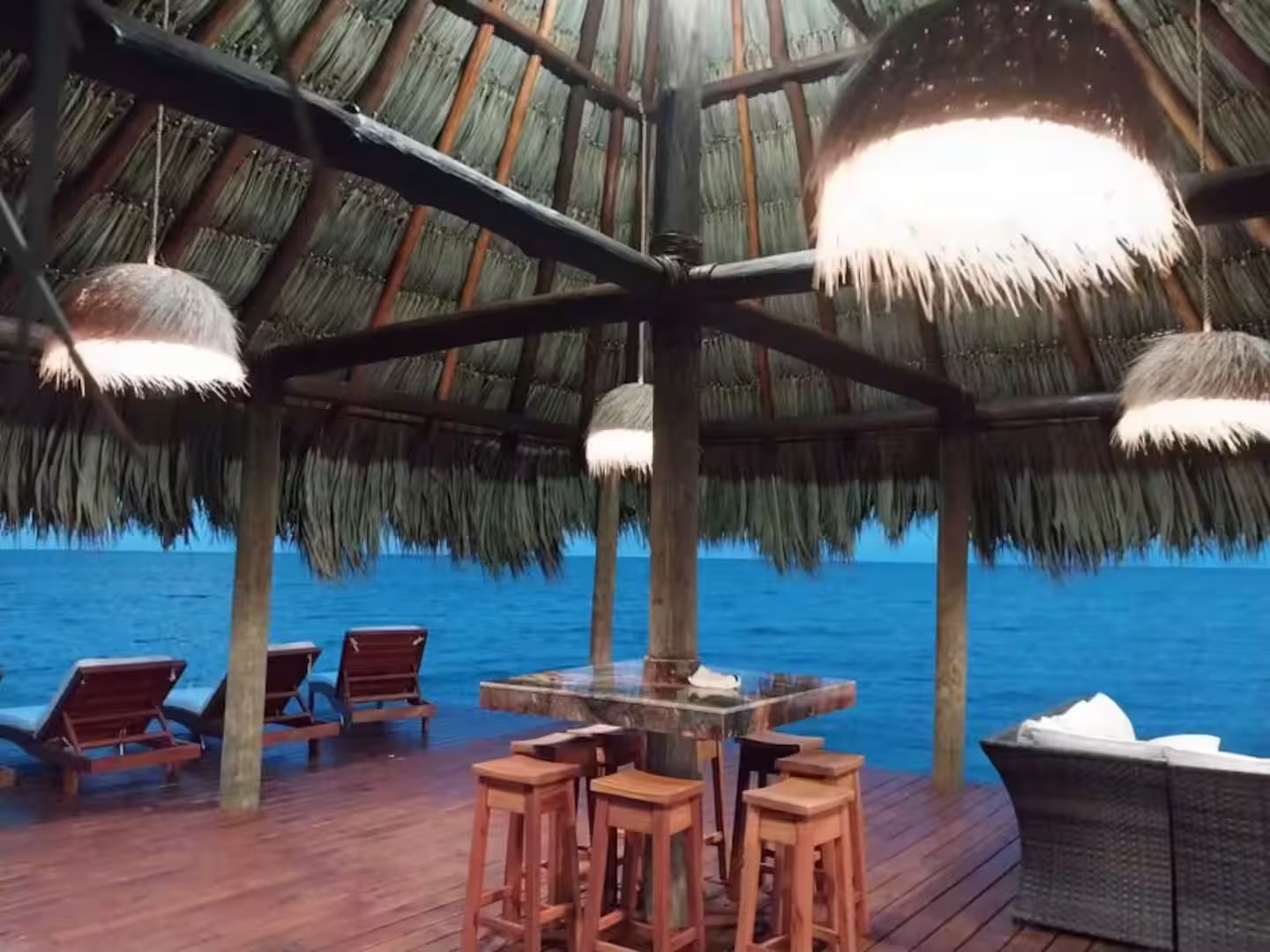 Eine Holzterrasse mit einem Reetdach, einer Bar und Liegestühlen mit Blick auf das Meer.