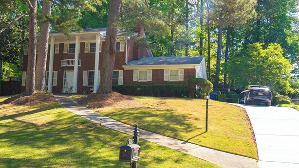 A two-story brick house with a front porch, a driveway, and a mailbox. - Elegant Home with Spacious Bedrooms & Lush Yard (East Point)