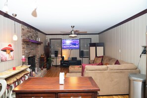 Ein Wohnzimmer mit einem Holztisch, einem beigefarbenen Sofa, einem Fernseher und einem Deckenventilator.