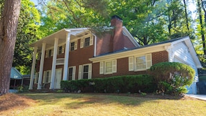A two-story brick house with a front porch, a chimney, and a well-maintained lawn. - Elegant Home with Spacious Bedrooms & Lush Yard (East Point)