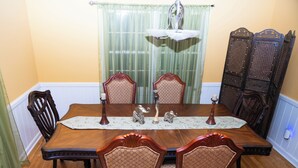 A dining room with a wooden table, four chairs, a chandelier, and a decorative panel. - Elegant Home with Spacious Bedrooms & Lush Yard (East Point)