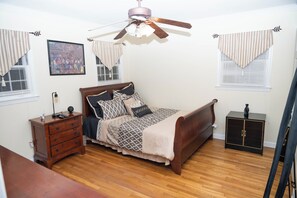 Ein Schlafzimmer mit einem Bett, einem Schminktisch, einem Nachttisch, einem Deckenventilator und einem Fenster mit Jalousien.