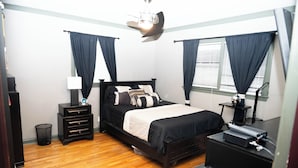 A bedroom with a bed, bedside tables, a lamp, a TV, and a window with curtains. - Elegant Home with Spacious Bedrooms & Lush Yard (East Point)