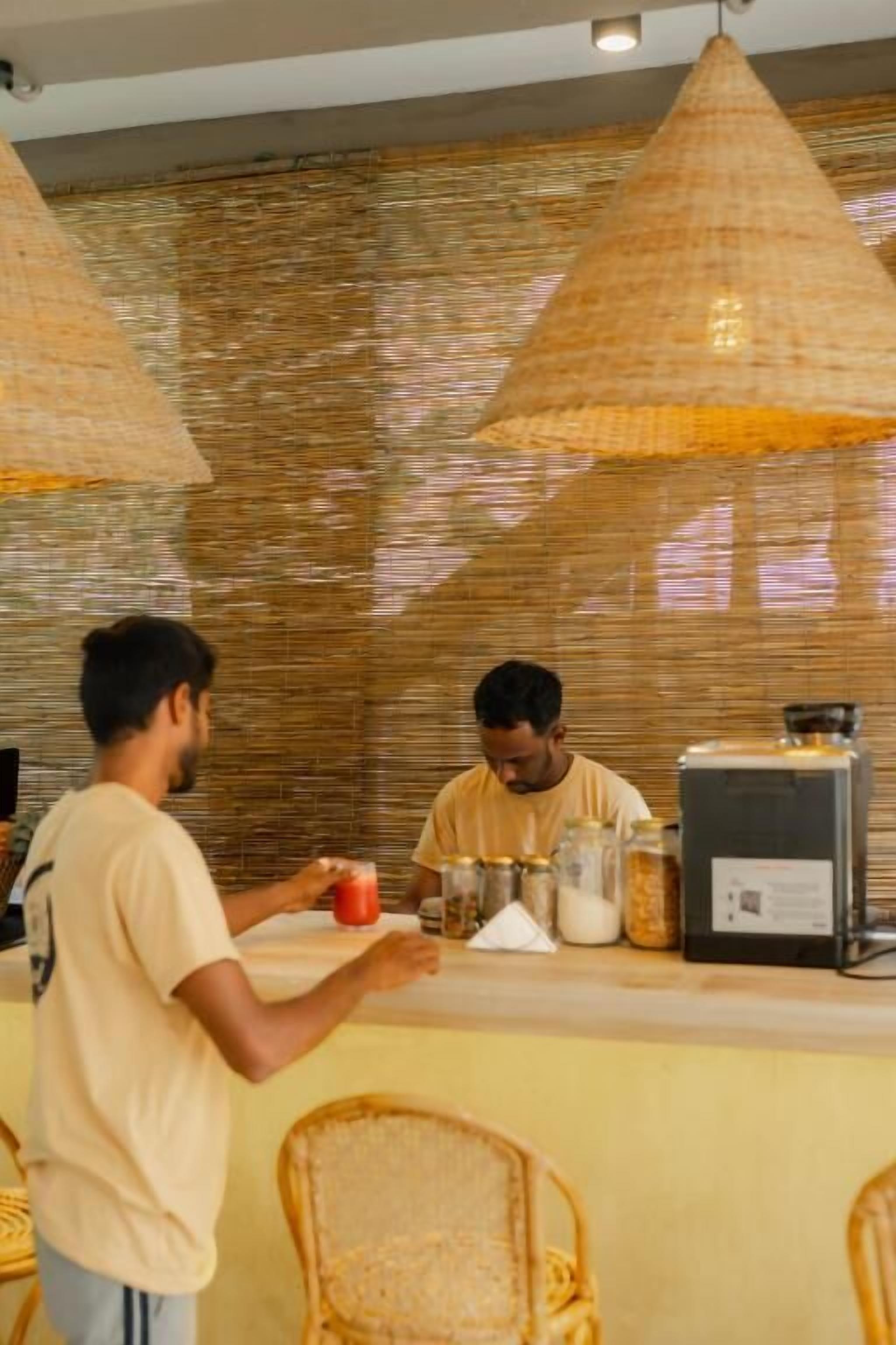 A cafe interior with a counter, wicker chairs, and hanging lamps.