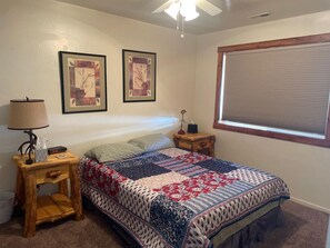 Ein Schlafzimmer mit einem Bett, einem Nachttisch, einer Lampe, einer Uhr und zwei gerahmten Bildern an der Wand.
