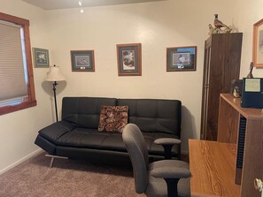 A living room with a black leather sofa, a grey armchair, a wooden cabinet, and framed pictures on the wall. - Cozy Mtn Home - 3-bedroom house in charming Bayfield near Durango & Pagosa Spgs (Bayfield)