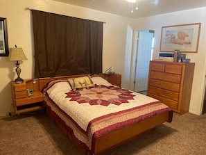 Un dormitorio con cama de madera, mesita de noche, cómoda, lámpara y un cuadro enmarcado en la pared.