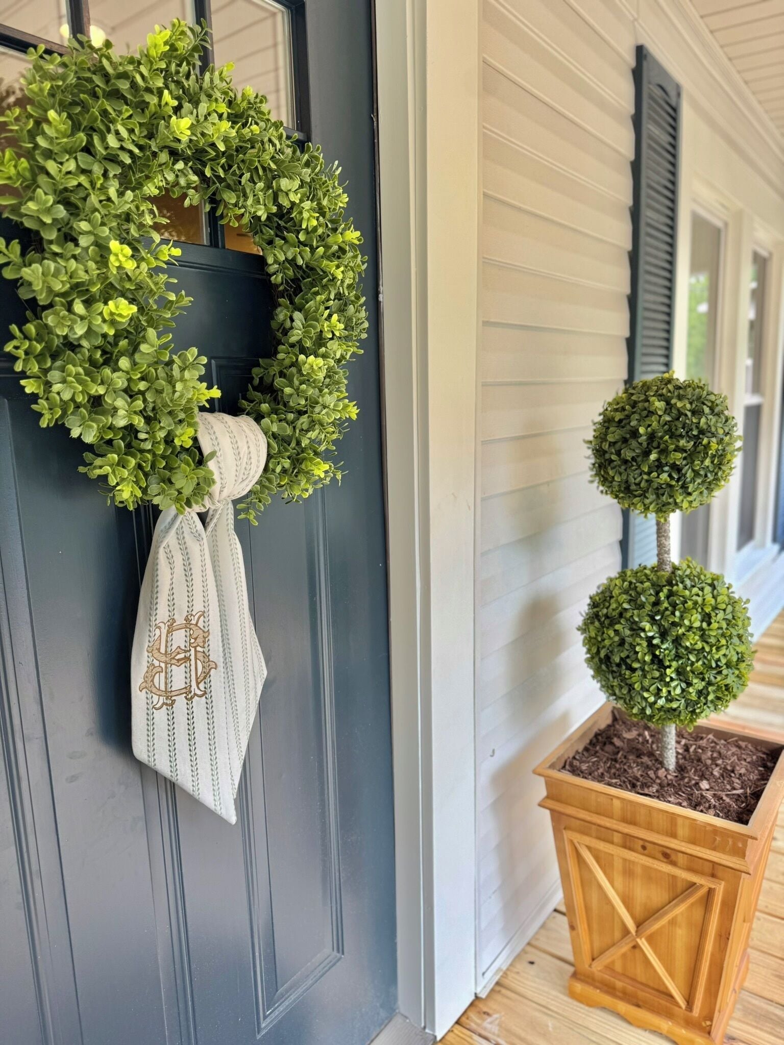 A front door with a wreath and a small potted tree.