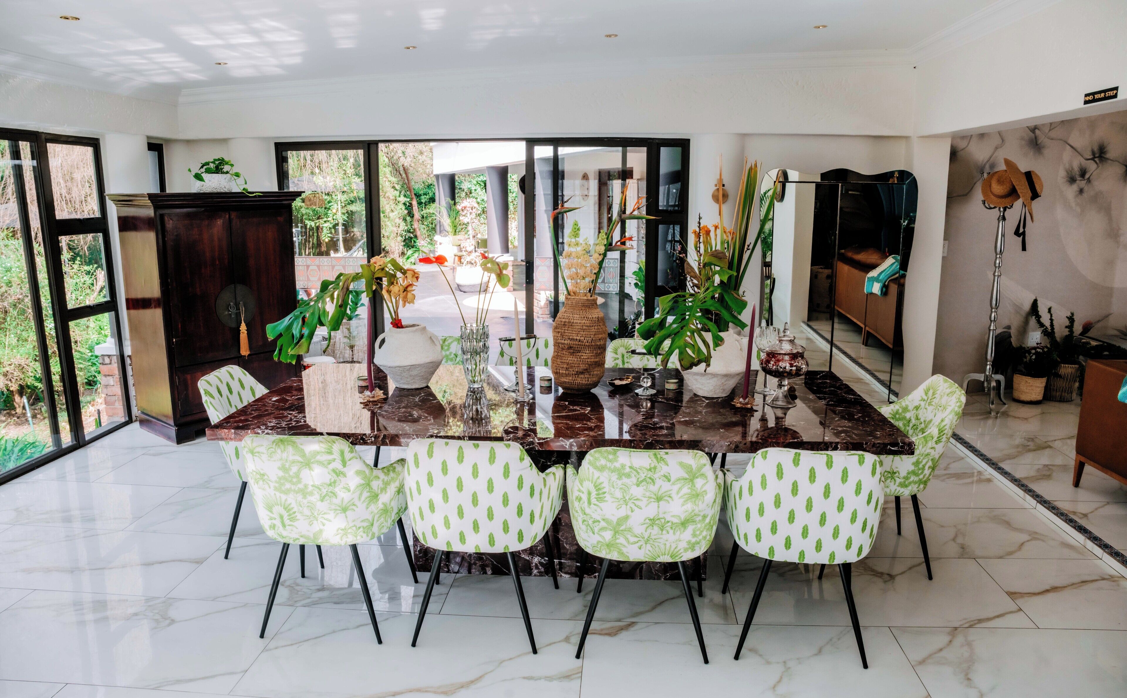 Un área de comedor con una mesa de mármol, sillas con estampado verde y plantas en macetas.