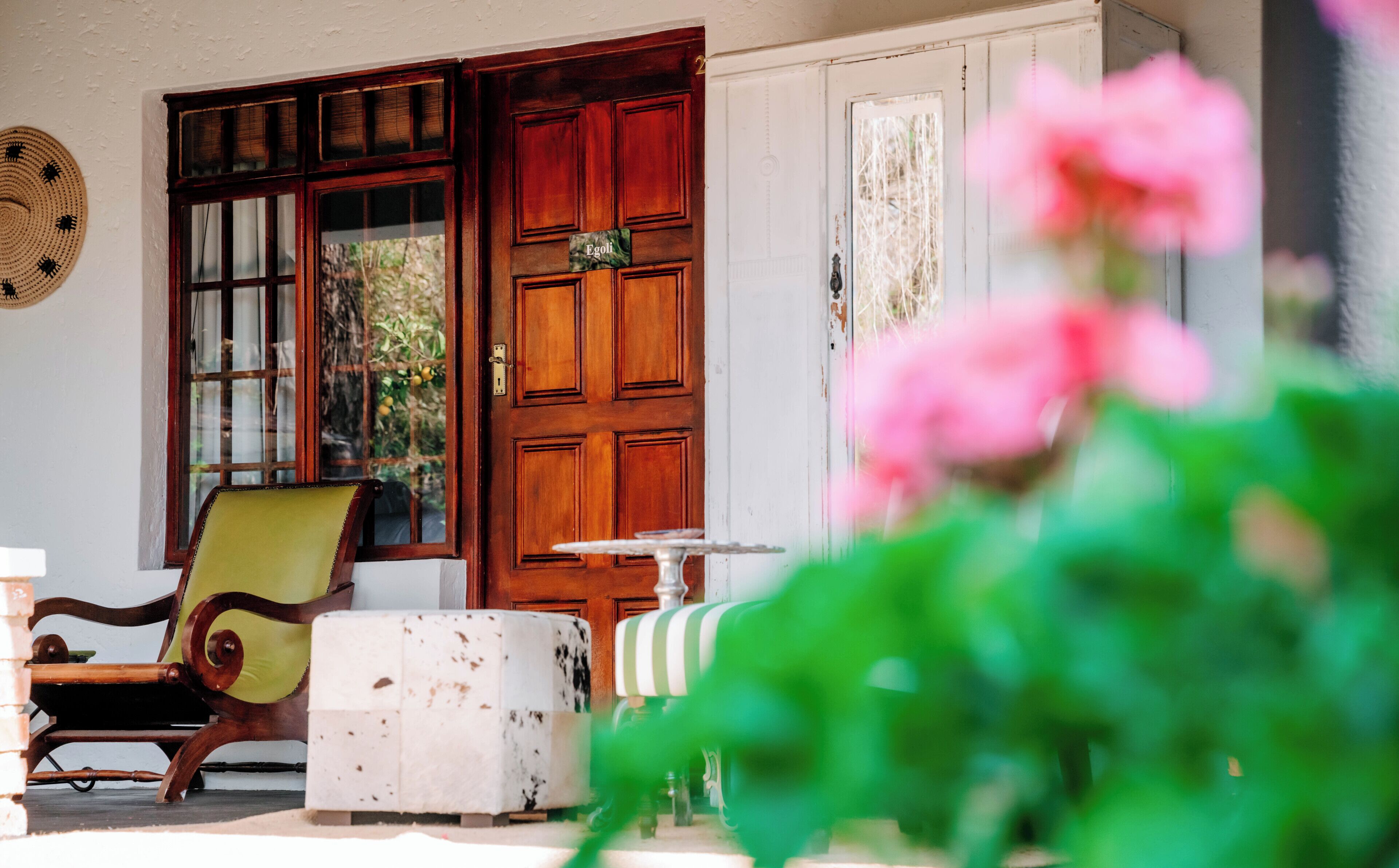 A room with a wooden door, a chair, a table, and a window with a view of greenery.
