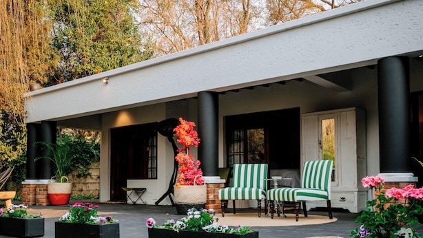 A covered outdoor seating area with a patio table, two chairs, and a basket of flowers.