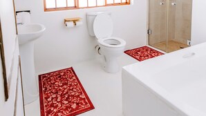 A bathroom with a toilet, sink, and bathtub. There is a window with a wooden frame and a shower area with glass doors.