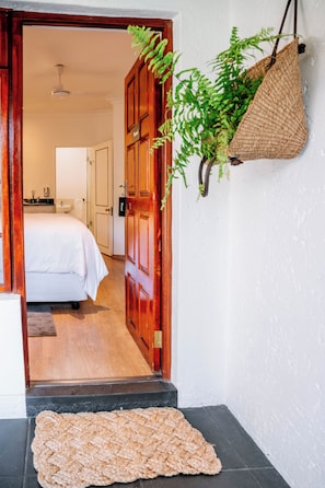 Ein Hotel Eingang mit einer Holztür, einer gewebten Matte und einer hängenden Pflanze.