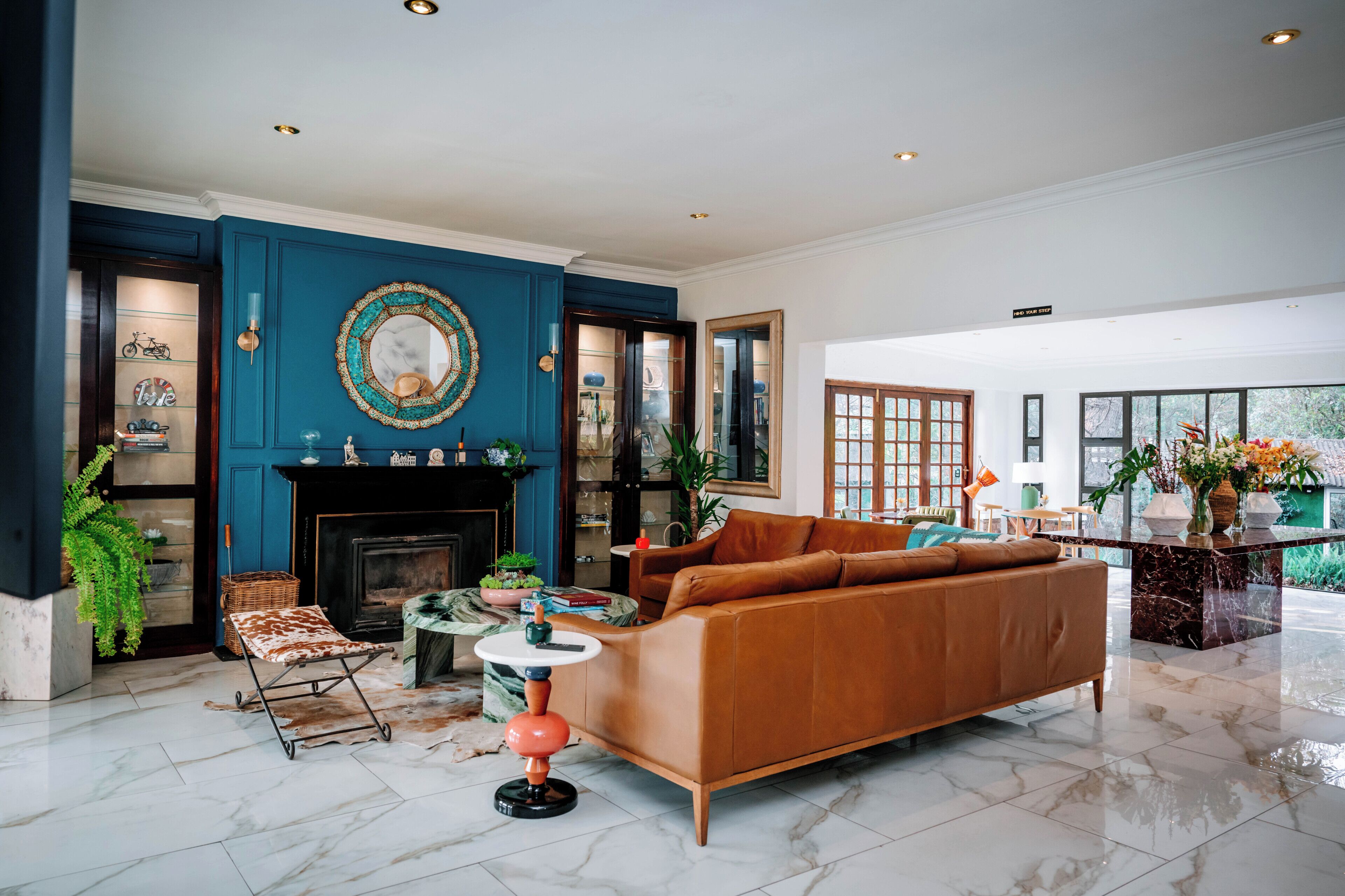 A living room with a blue accent wall, a fireplace, a leather sofa, and a dining area with a view.