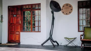 Una puerta de madera tradicional con una placa, una gran escultura metálica, un sombrero tejido y una silla verde acolchada.