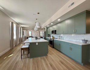 A modern kitchen with a central island, stainless steel appliances, and light green cabinetry.