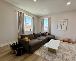 A modern living room with a brown sectional sofa, a white coffee table, and a patterned rug.