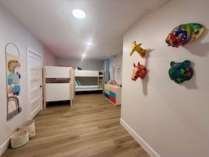 A child's room with bunk beds, a wall with colorful animal decorations, and a door with a rainbow-themed curtain.