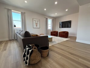 A modern living room with a sofa, two armchairs, a coffee table, and a flat-screen TV mounted on the wall.