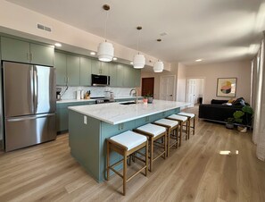 A modern kitchen with a central island, bar stools, stainless steel appliances, and pendant lighting.