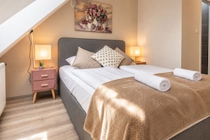 A bedroom with a bed, two bedside tables, a nightstand, a lamp, and a painting on the wall.