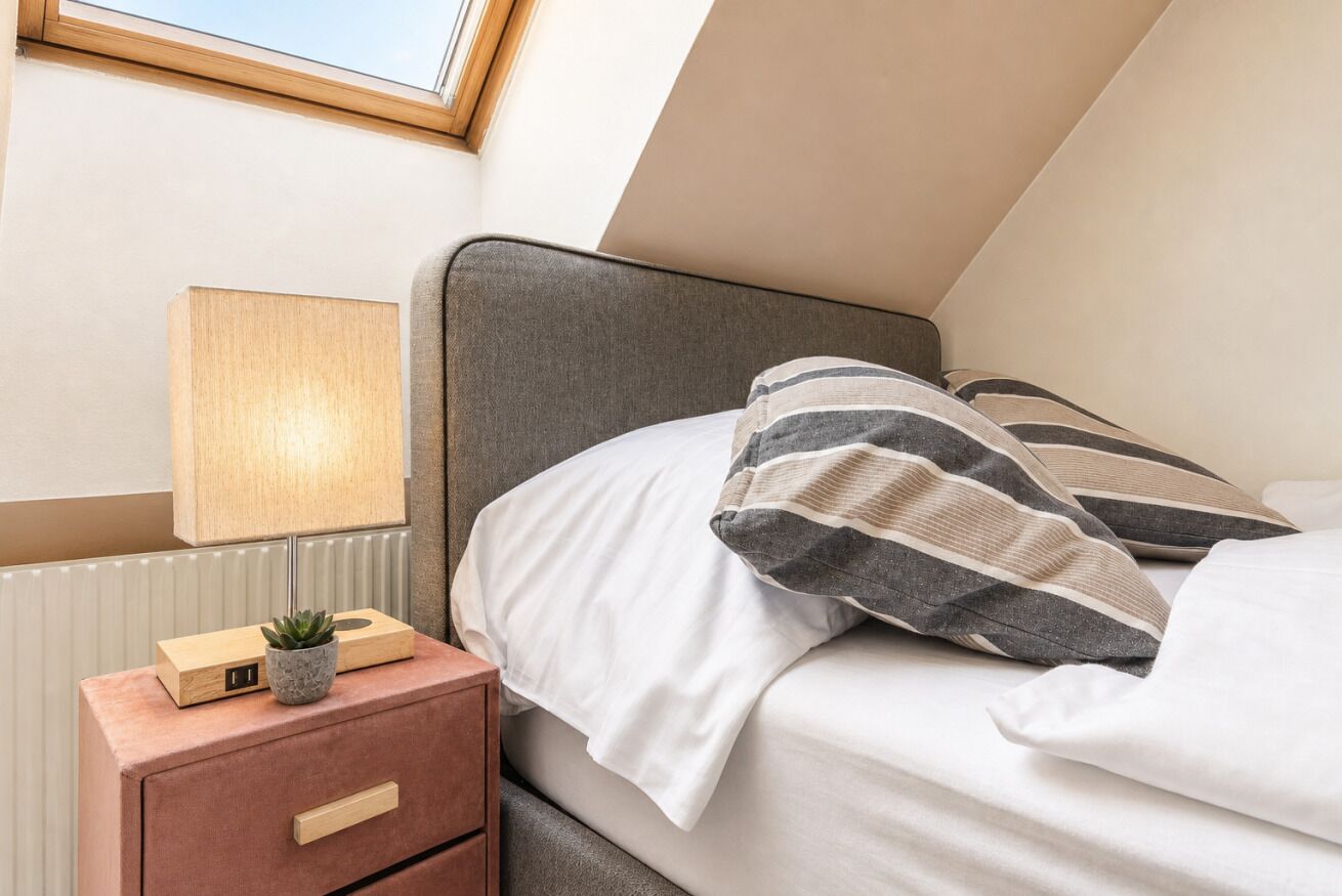 Une chambre à coucher avec un lit, une table de chevet avec une lampe, une petite plante et un tiroir.