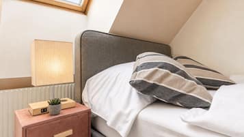 Une chambre à coucher avec un lit, une table de chevet avec une lampe, une petite plante et un tiroir.