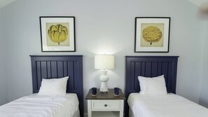 A hotel room with two beds, a nightstand between them, and two framed botanical prints on the wall.